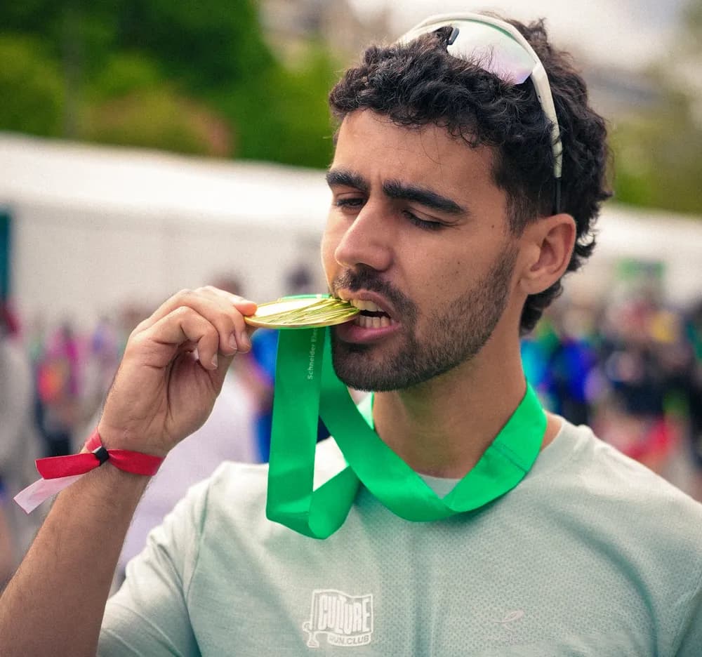 Un coureur mord sa médaille à l’arrivée, sourire aux lèvres
