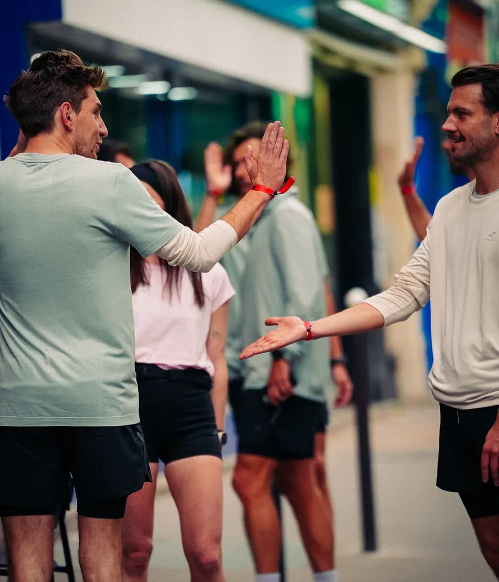Deux coureurs se tapent dans la main au milieu du groupe, devant un magasin Intersport