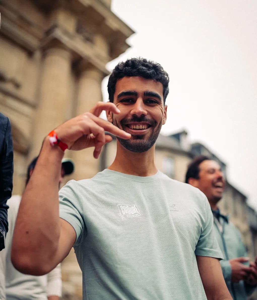 Un coureur souriant fait un signe de la main vers l’objectif, ses coéquipiers derrière lui